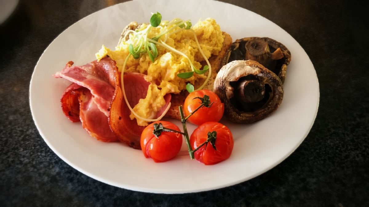 A cooked breakfast: bacon, scrambled eggs, mushrooms and roast tomatoes